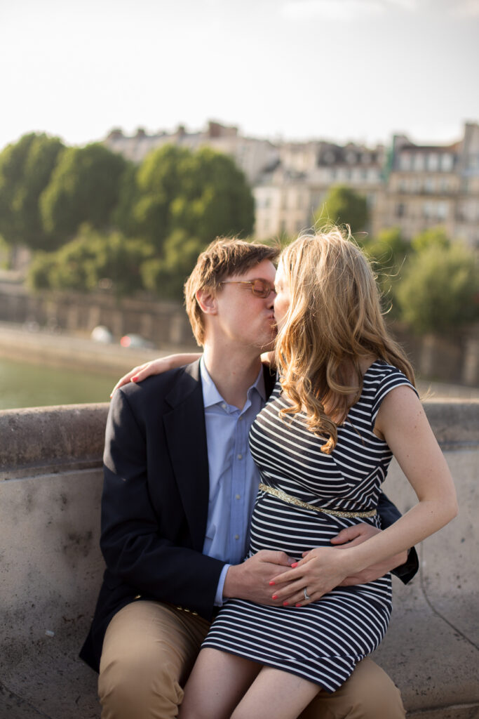 Expecting couple cuddling on a wall by the Seine during a maternity photoshoot in Paris