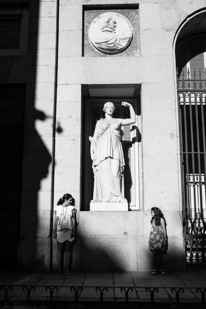 Black and white photo of a mother and daughter mimicking a statue's pose at the Prado Museum in Madrid