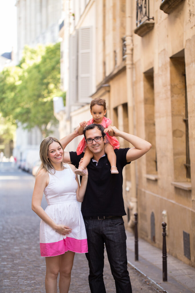 Dad carrying his daughter on his shoulders as the family laughs on a Paris street