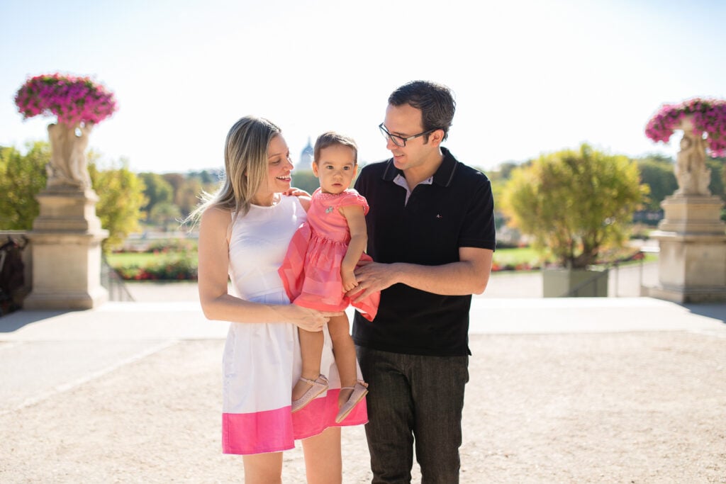 Family of three standing together in a Paris garden with flower urns behind them