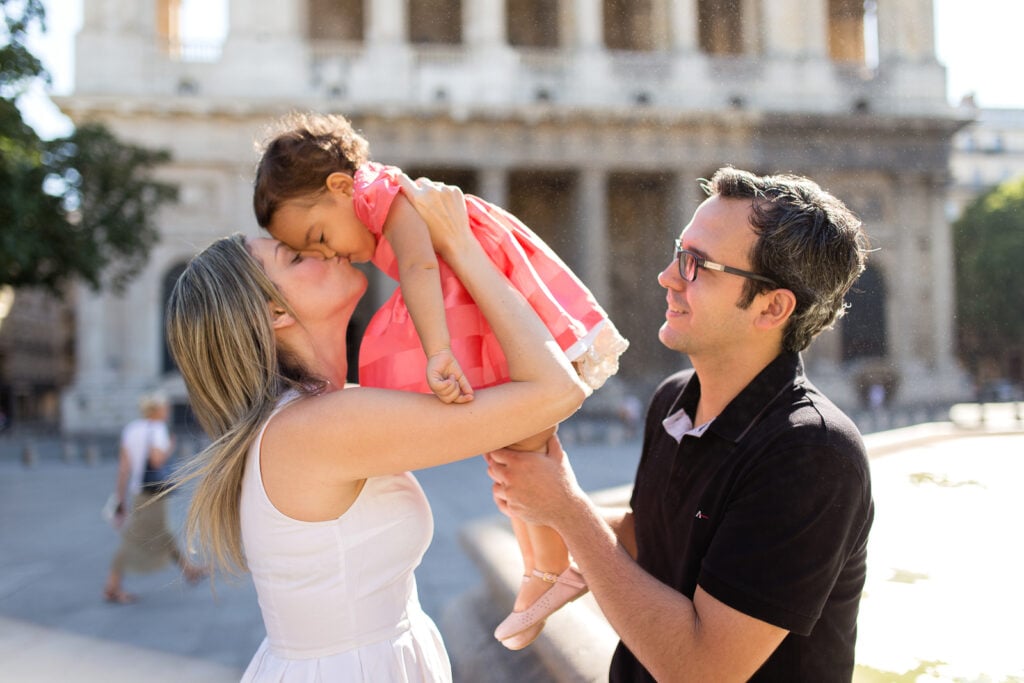 Mom kissing her daughter as she holds her up, with Dad smiling beside them