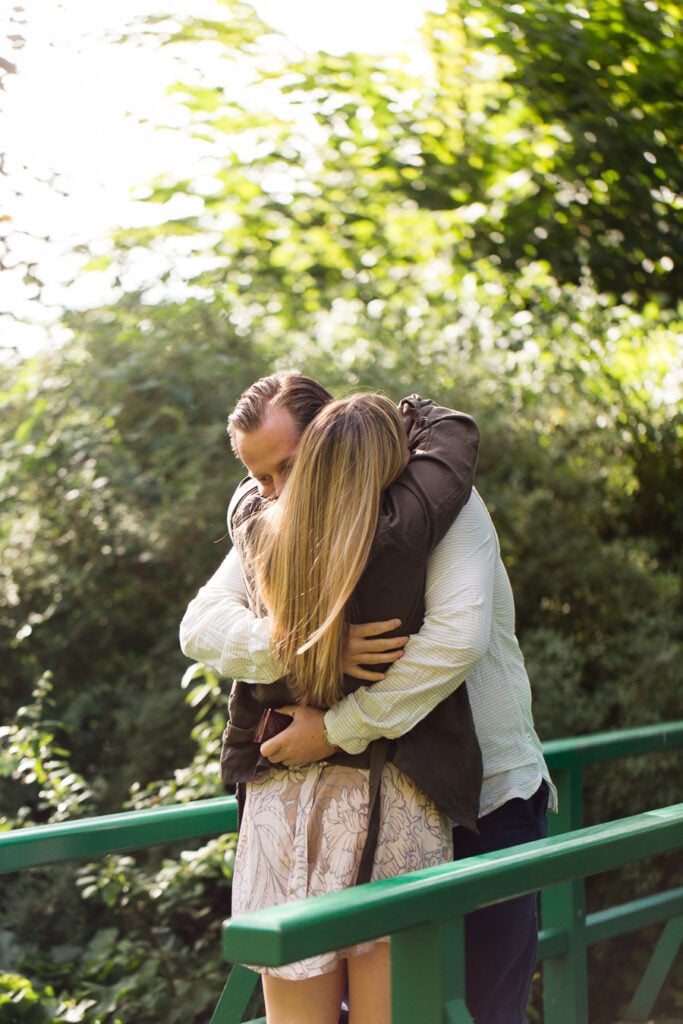 Newly engaged couple hugging on the green bridge in Monet's water lily garden