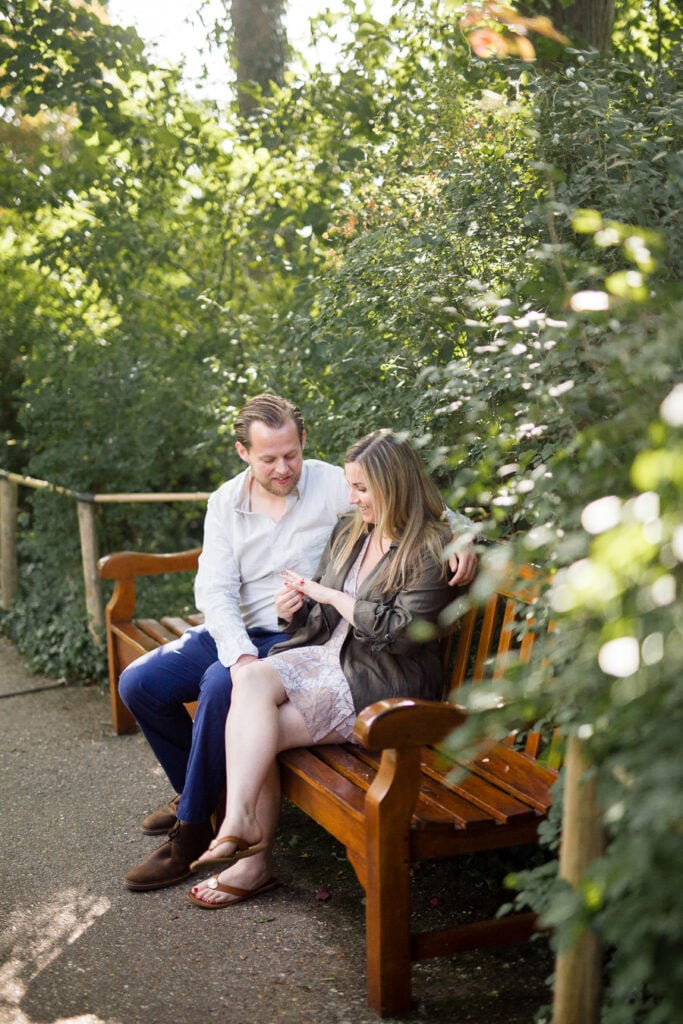 Engaged couple sitting on a wooden bench surrounded by greenery in Monet's garden