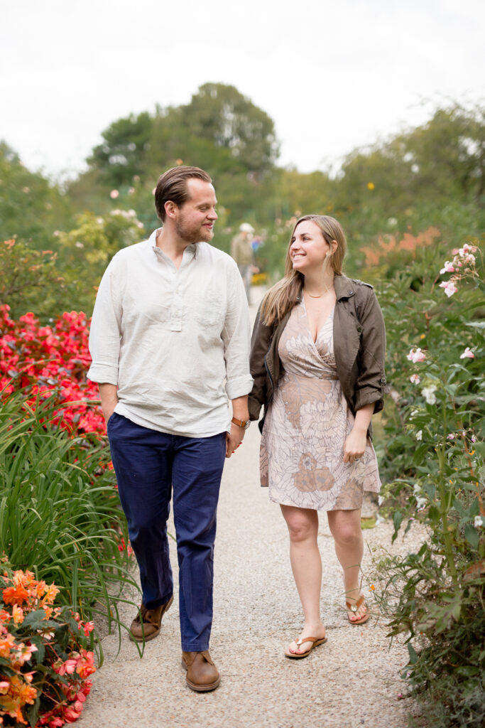 Engaged couple walking hand in hand along a flower-lined path in Giverny