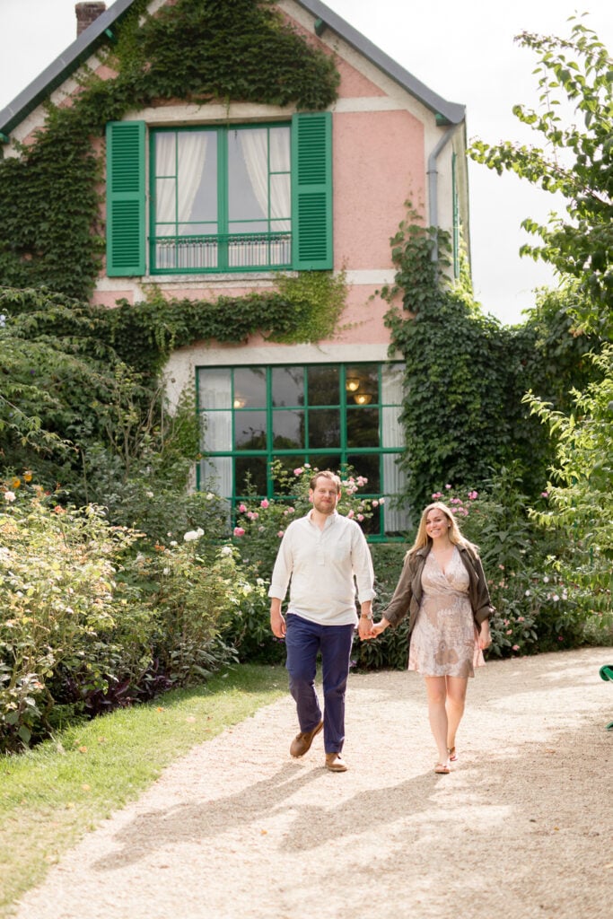 Engaged couple walking in front of Monet's pink house with green shutters in Giverny