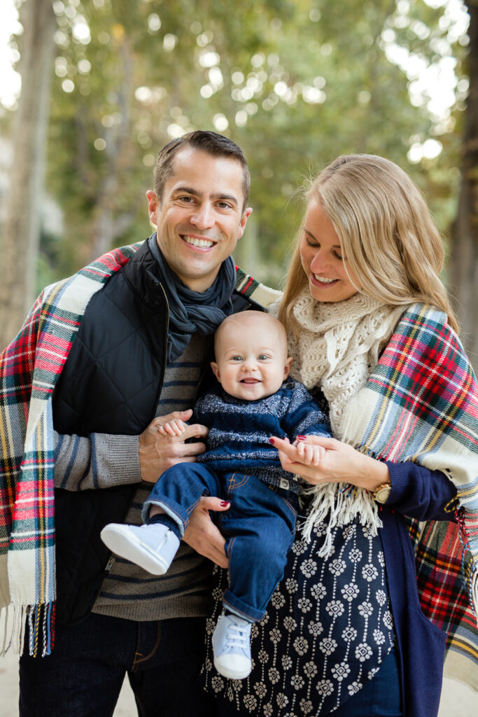 Family of three wrapped in a tartan blanket in layered fall outfits in Paris