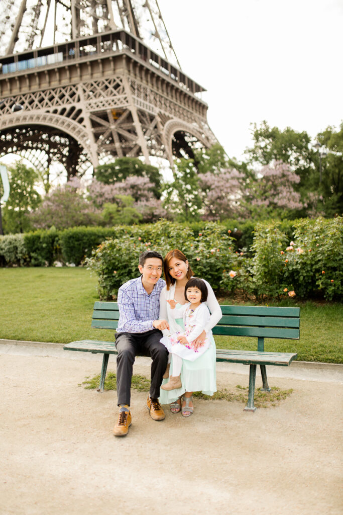 Family of three sitting on a green bench under the Eiffel Tower in Paris