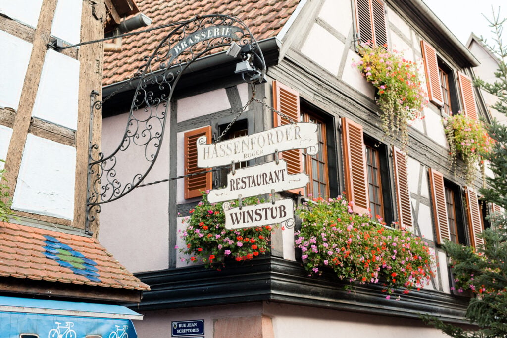Restaurant and winstub signs on a flower-covered half-timbered house in Kaysersberg