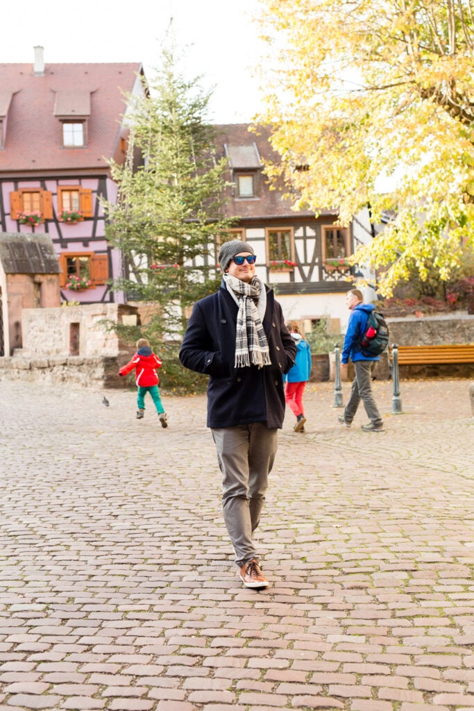 Man in a scarf walking across a cobblestone square in Kaysersberg, Alsace