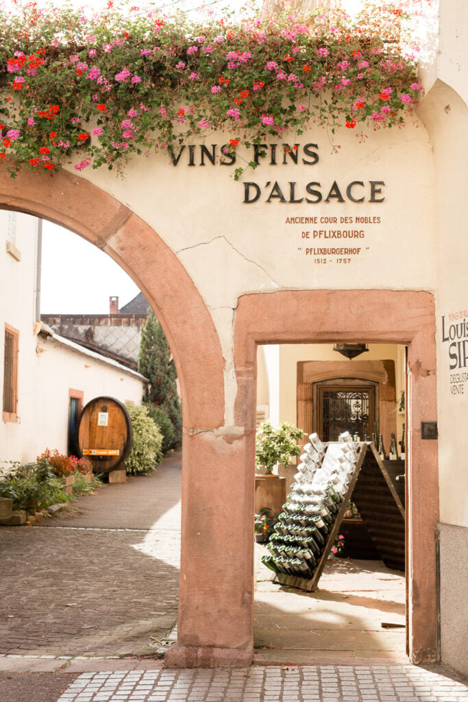 Stone archway with a Vins Fins d'Alsace sign and flower boxes in Ribeauvillé, Alsace