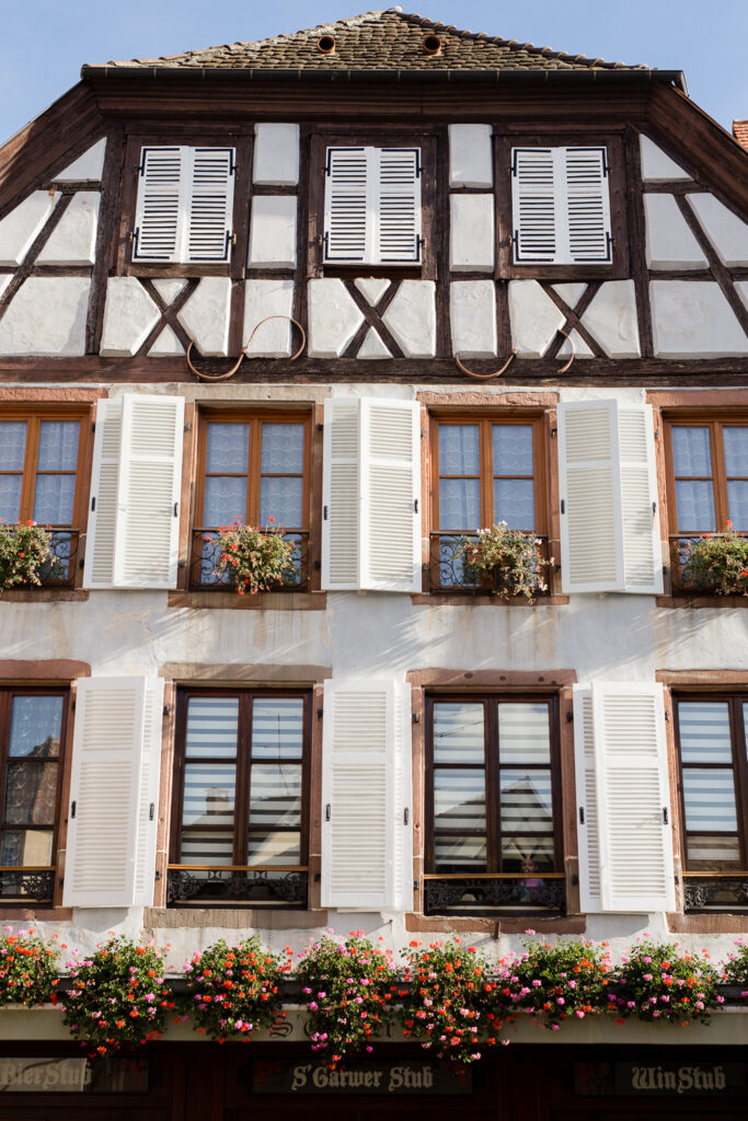 Traditional half-timbered house with white shutters and flower boxes in Ribeauvillé