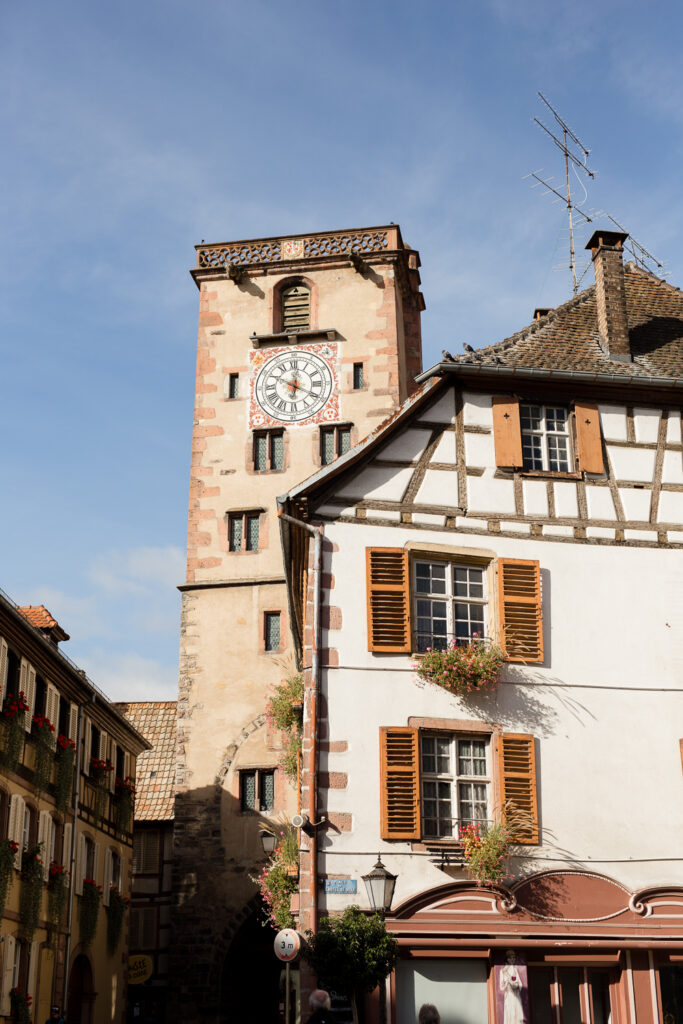 Clock tower and half-timbered houses under a blue sky in Ribeauvillé, Alsace