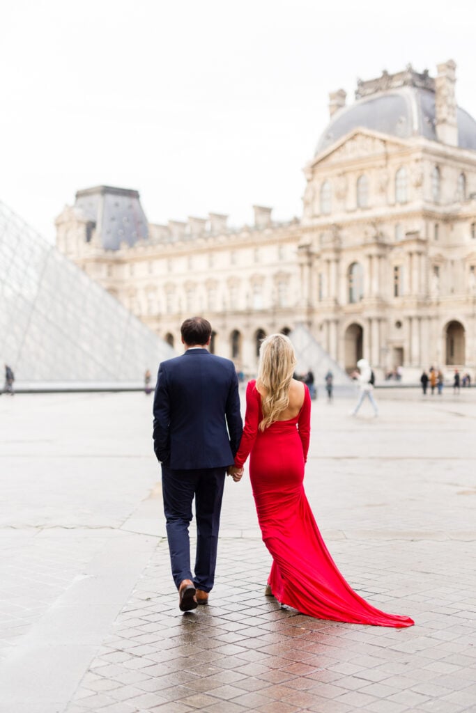Expecting couple walking hand in hand toward the Louvre pyramid on a rainy morning