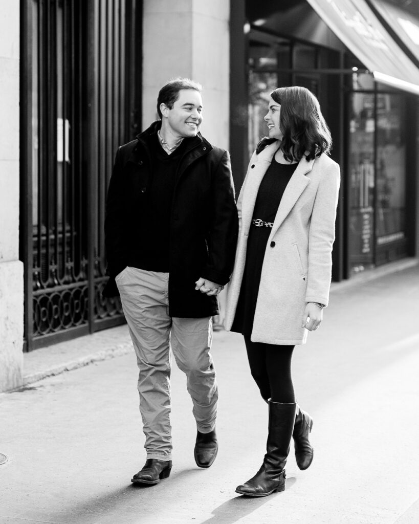 Black and white photo of a couple walking and laughing on a Paris street near the Eiffel Tower