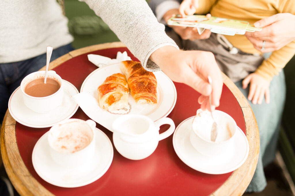 Hands reaching for croissants and hot chocolate on a red café table in Paris