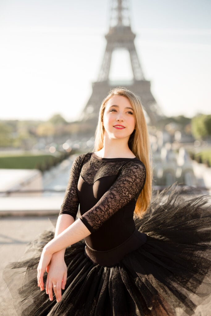 Teen ballerina in a black lace leotard and tutu posing with the Eiffel Tower behind her