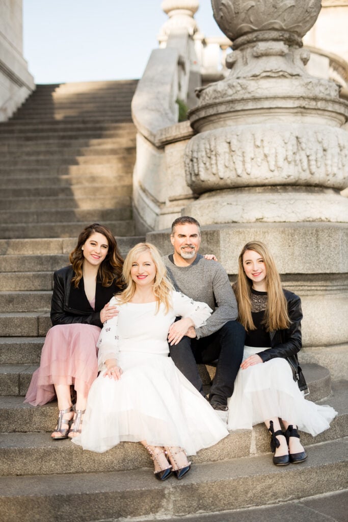 Family of four sitting together on stone steps in Paris, daughters in tulle skirts