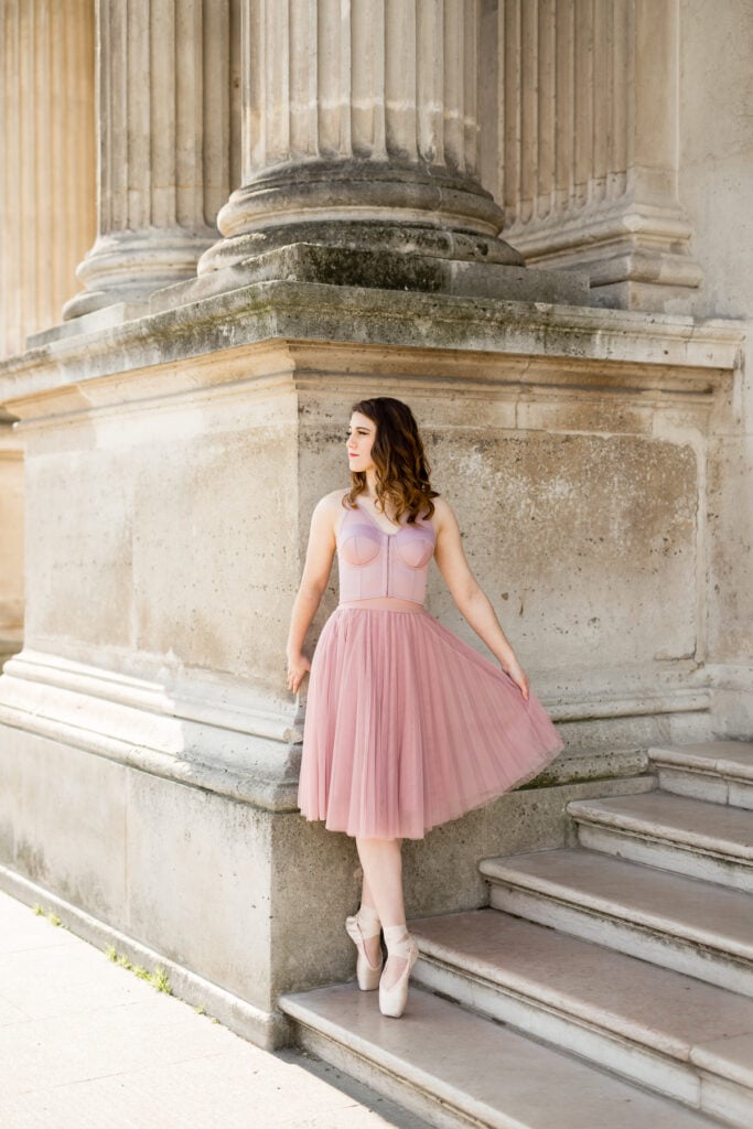 Ballerina en pointe in a pink tulle dress beside stone columns in Paris