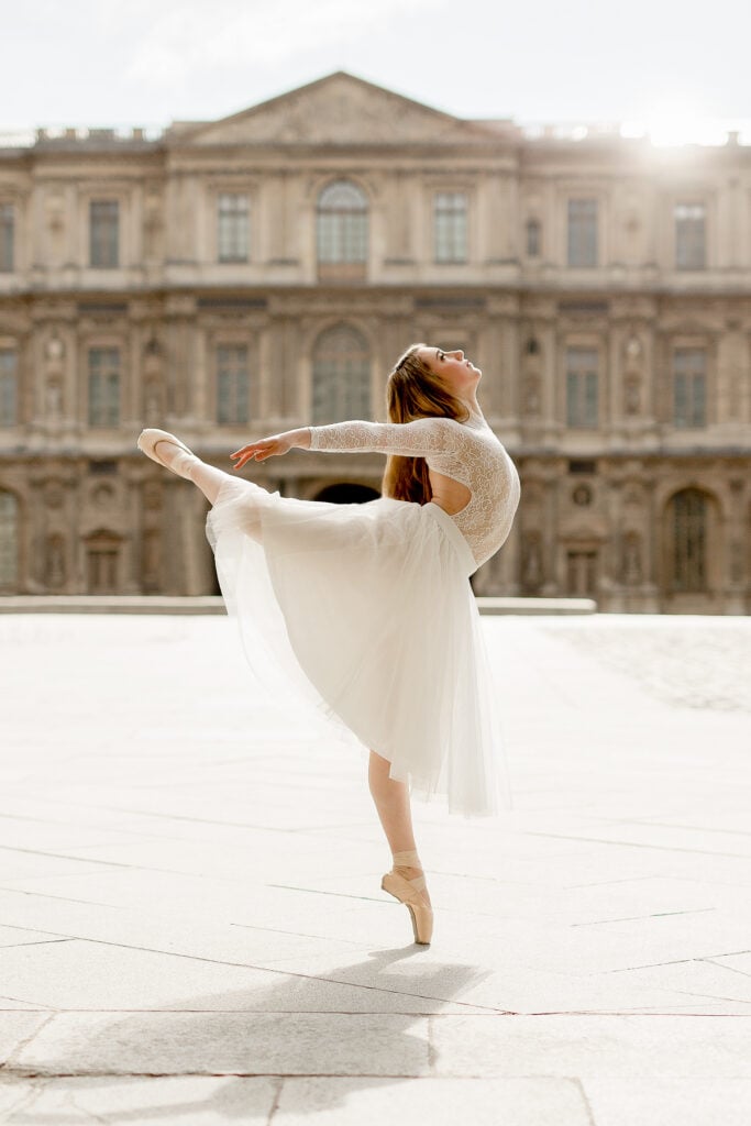 Ballerina in a white dress in an arabesque en pointe in a courtyard of the Louvre in Paris