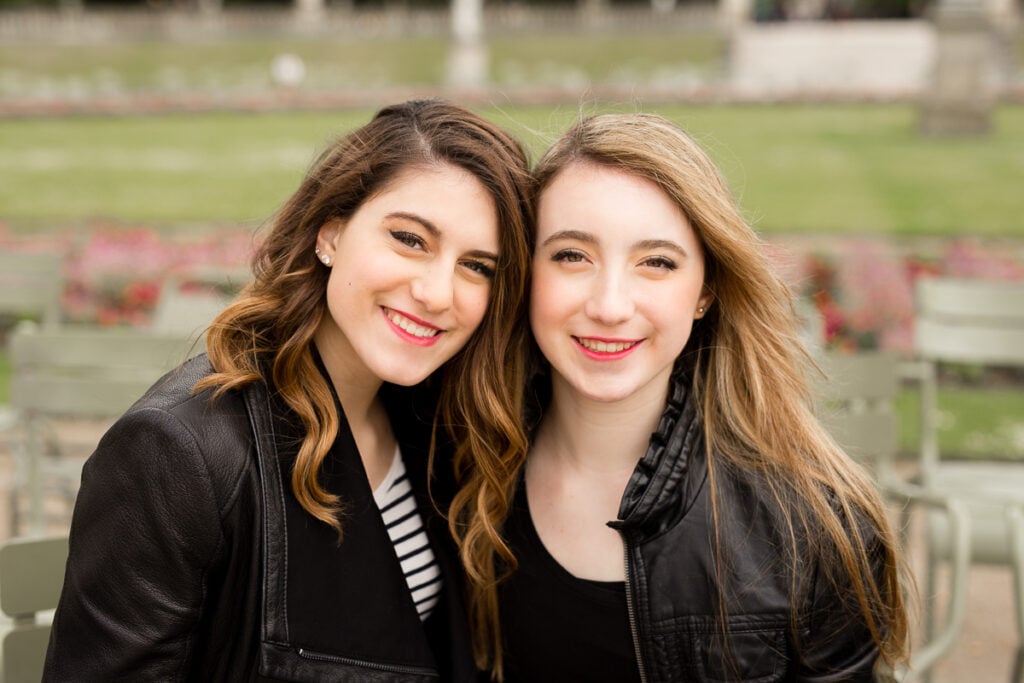 Two sisters in black leather jackets smiling cheek to cheek in a Paris garden