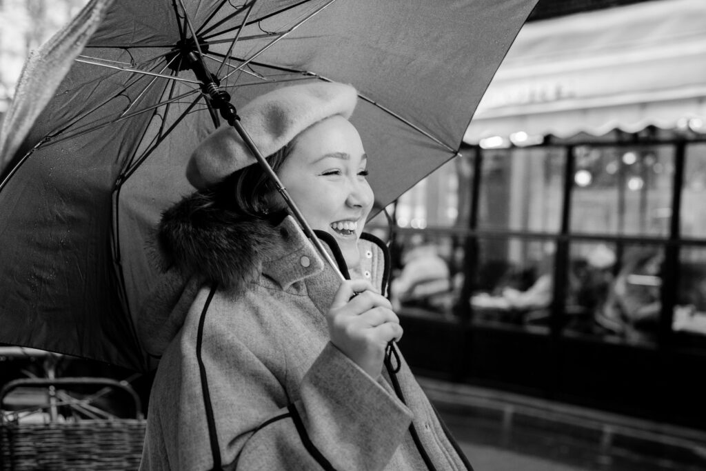 Black and white portrait of woman walking down street with umbrella on rainy day in Paris by Katie Donnelly Photography