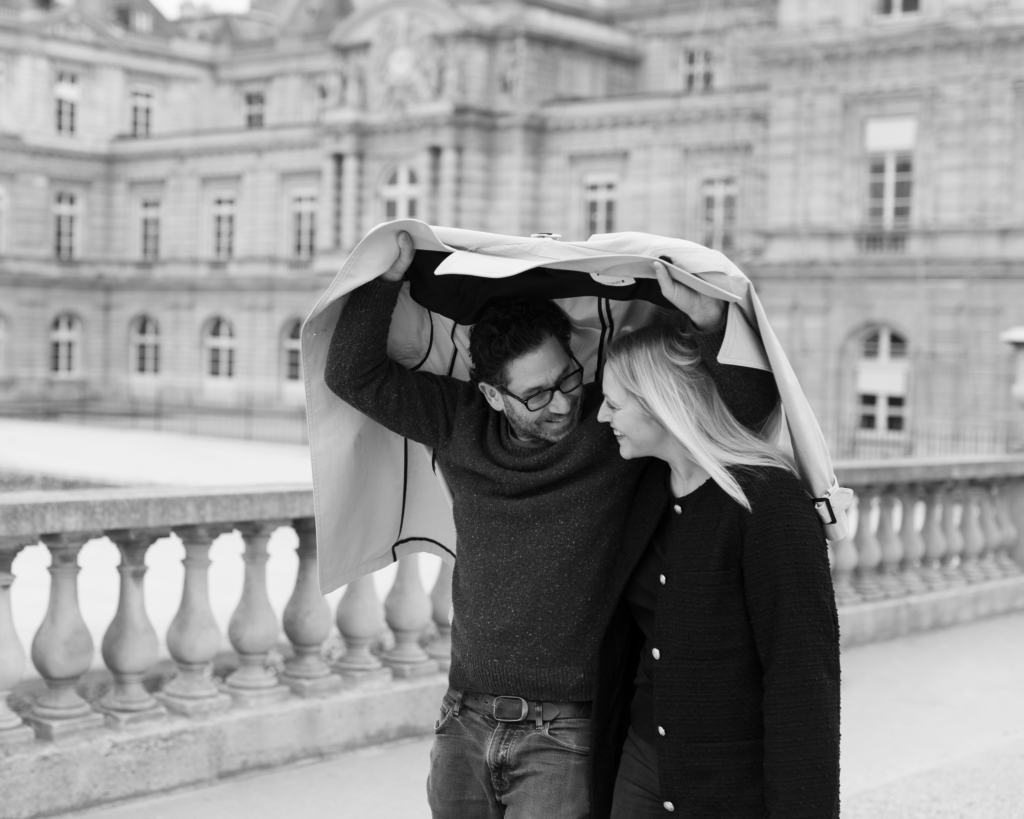 Black and white portrait of couple walking together in Paris under coat on rainy day by Katie Donnelly Photography