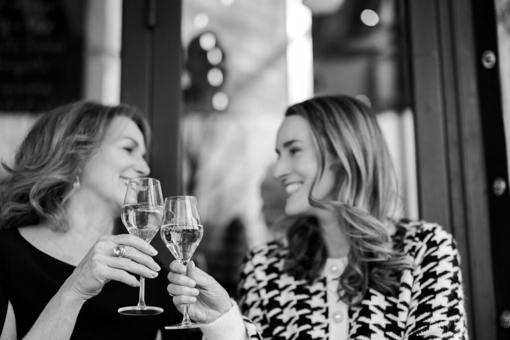 Black and white portrait of mother and adult daughter clinking wine glasses in Paris: Paris in July 2026: Bastille Day Celebrations by Katie Donnelly Photography