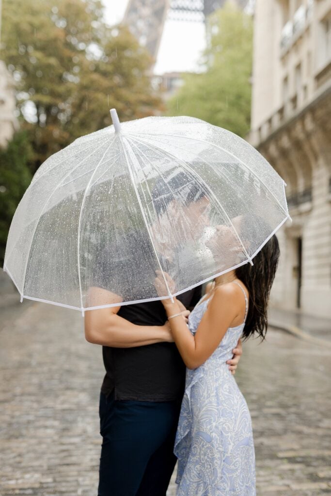 Portrait of young couple kissing under clear umbrella on rainy day in Paris: Fall Packing Guide by Katie Donnelly Photography