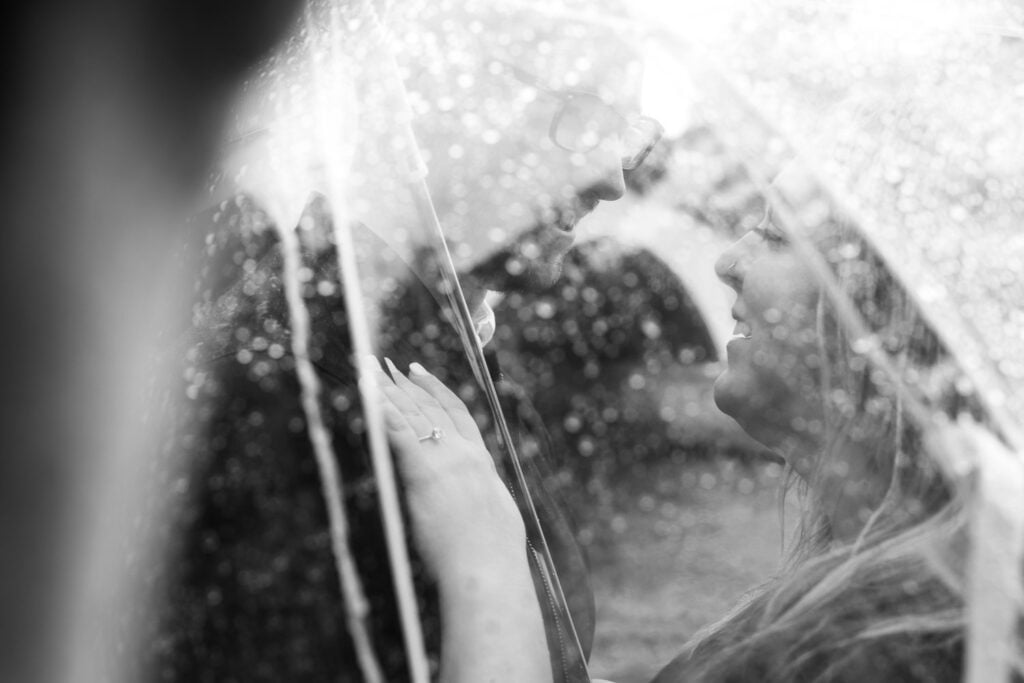 Black and white portrait of couple under clear umbrella on Paris rainy day photoshoot by Katie Donnelly Photography
