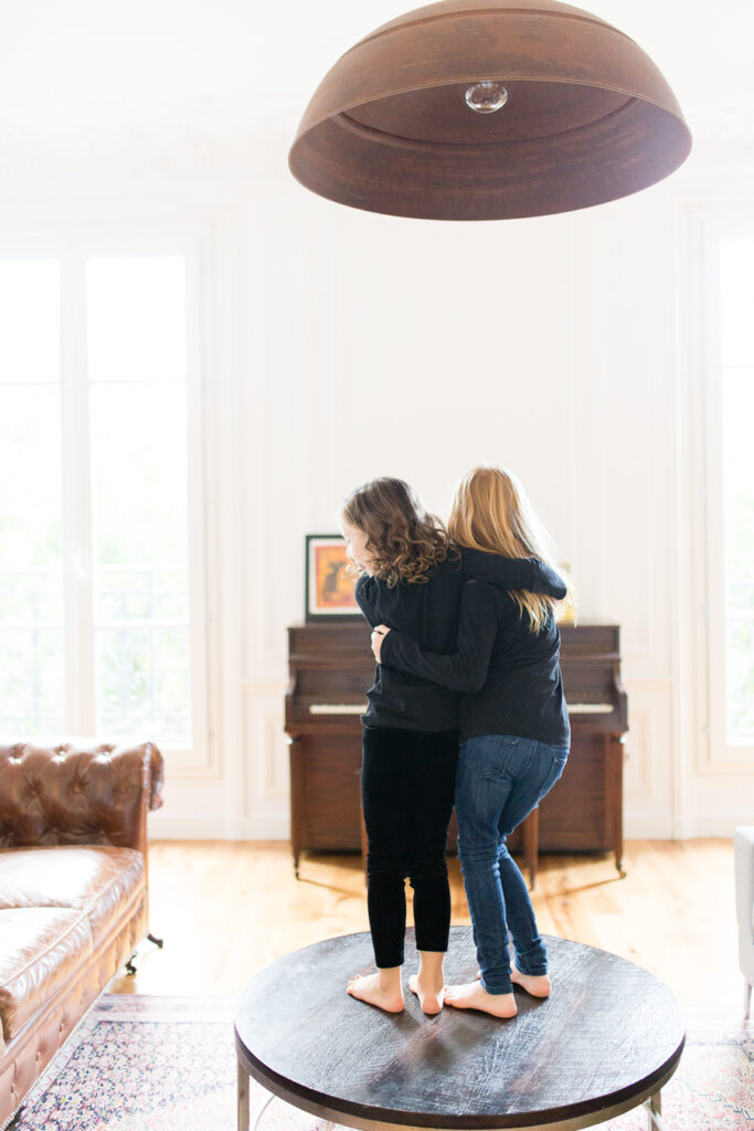 Mother hugging her daughter as they dance on a table in a bright living room