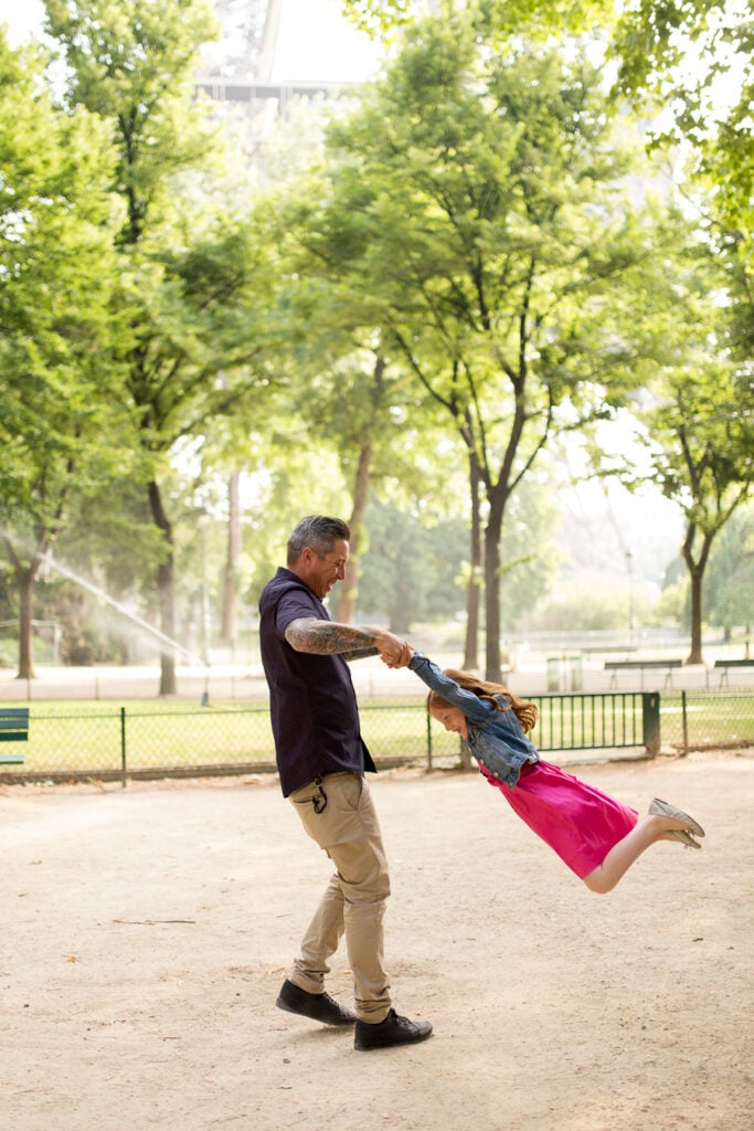 Dad swinging his daughter around by the arms in a Paris park, frozen in motion