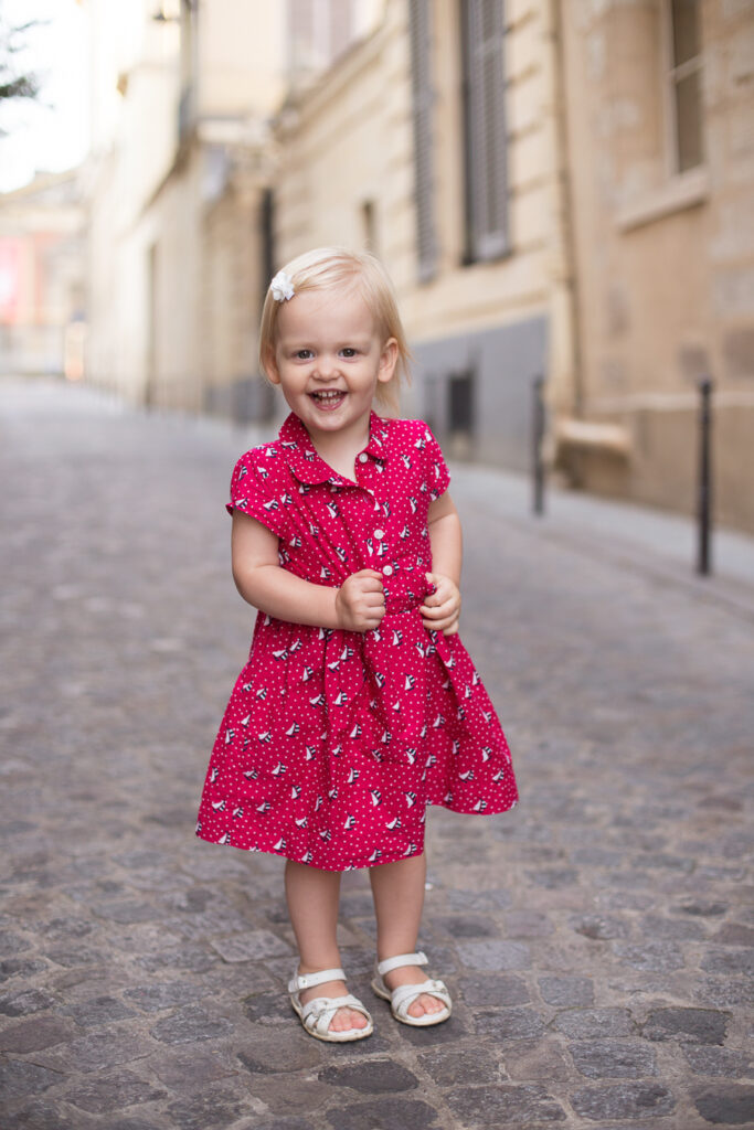 Little girl in a red dress standing on a cobblestone street in Paris, photographed from her eye level so she looks big