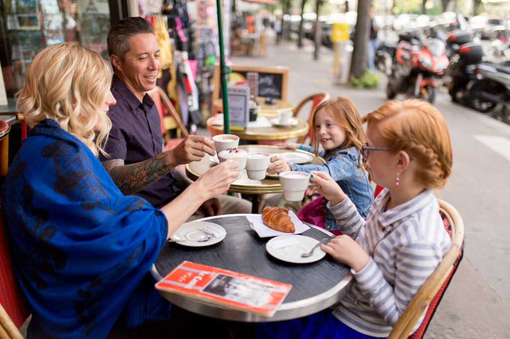 Family laughing together around a table at a Paris café terrace