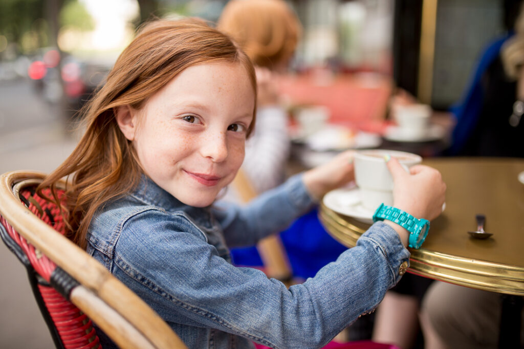 Red-haired girl smiling at the camera at a Paris café table