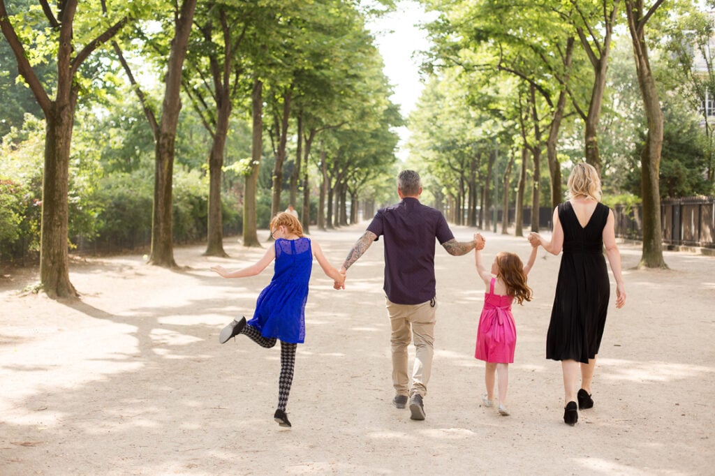 Family of four holding hands and walking down a tree-lined alley in the Champ de Mars