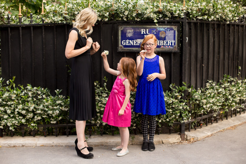Mother and two daughters in bright dresses laughing beside a Paris street sign