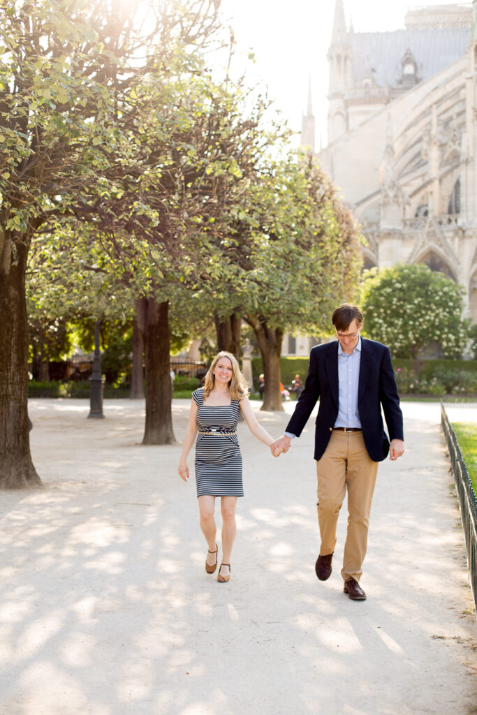 Expecting couple walking hand in hand under the trees beside Notre-Dame in Paris