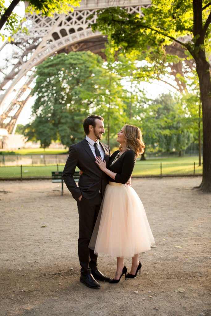 Couple embracing under the trees at the foot of the Eiffel Tower during a honeymoon photoshoot in Paris