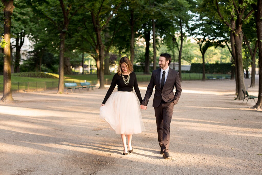 Couple walking hand in hand along a tree-lined path near the Eiffel Tower