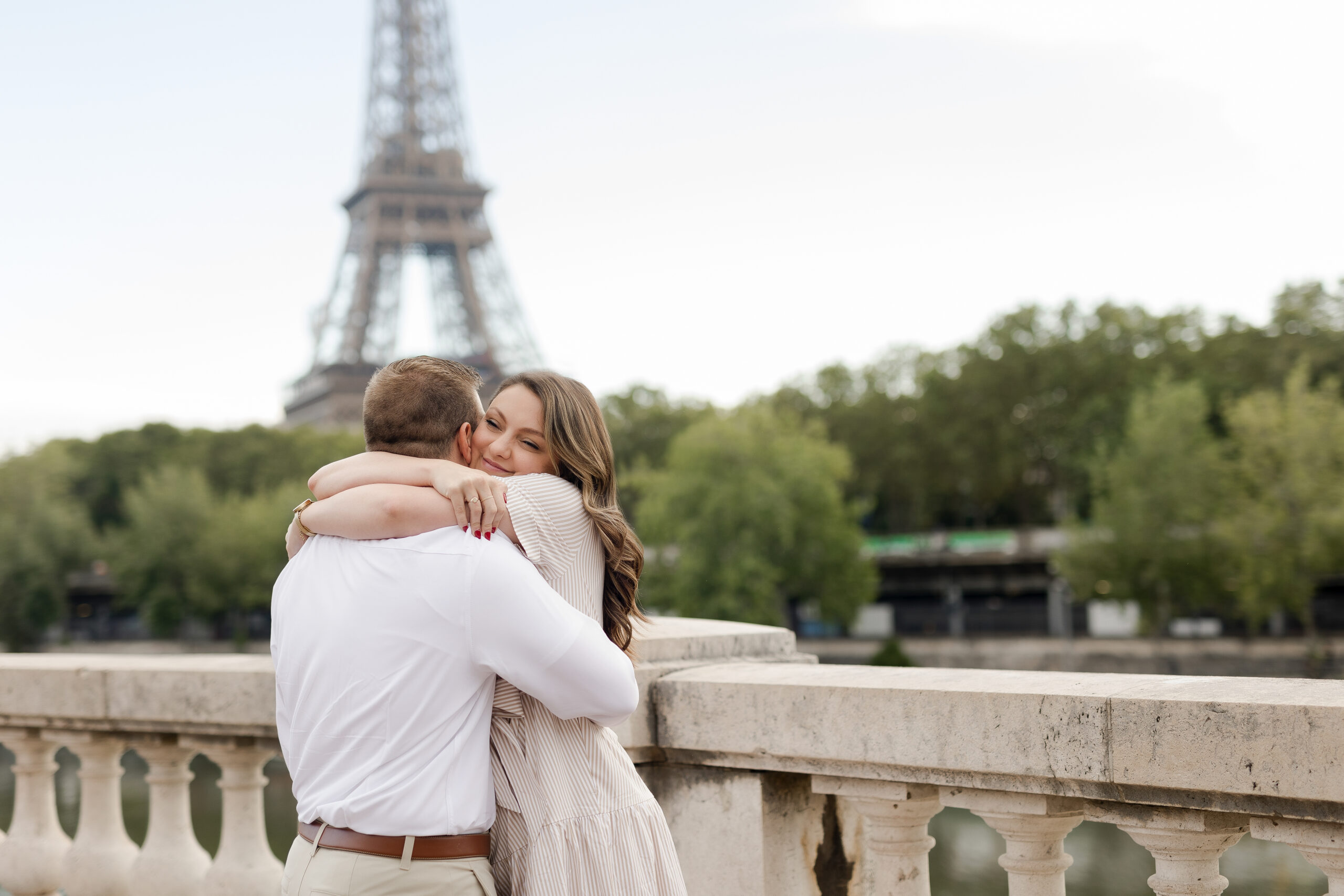 A romantic couple photoshoot on Bir Hakeim Bridge in Paris, captured by Katie Donnelly Photography. The couple is posing under the iconic bridge with the Eiffel Tower in the background.