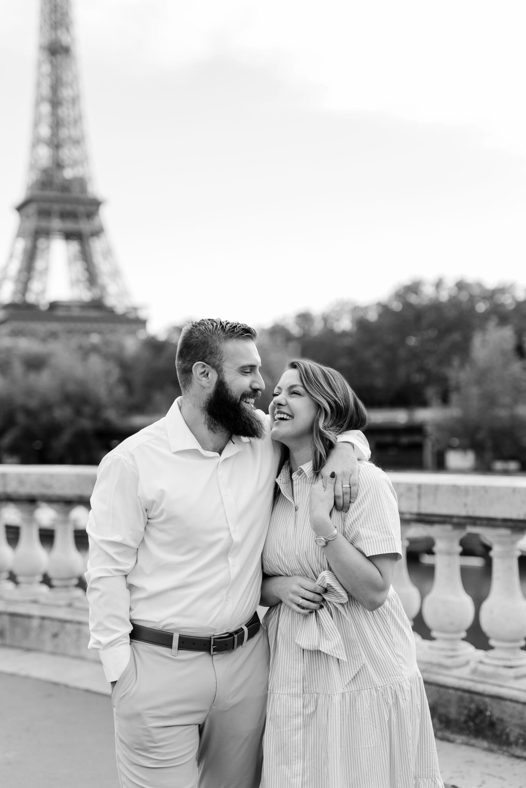 A romantic couple photoshoot on Bir Hakeim Bridge in Paris, captured by Katie Donnelly Photography. The couple is posing under the iconic bridge with the Eiffel Tower in the background.