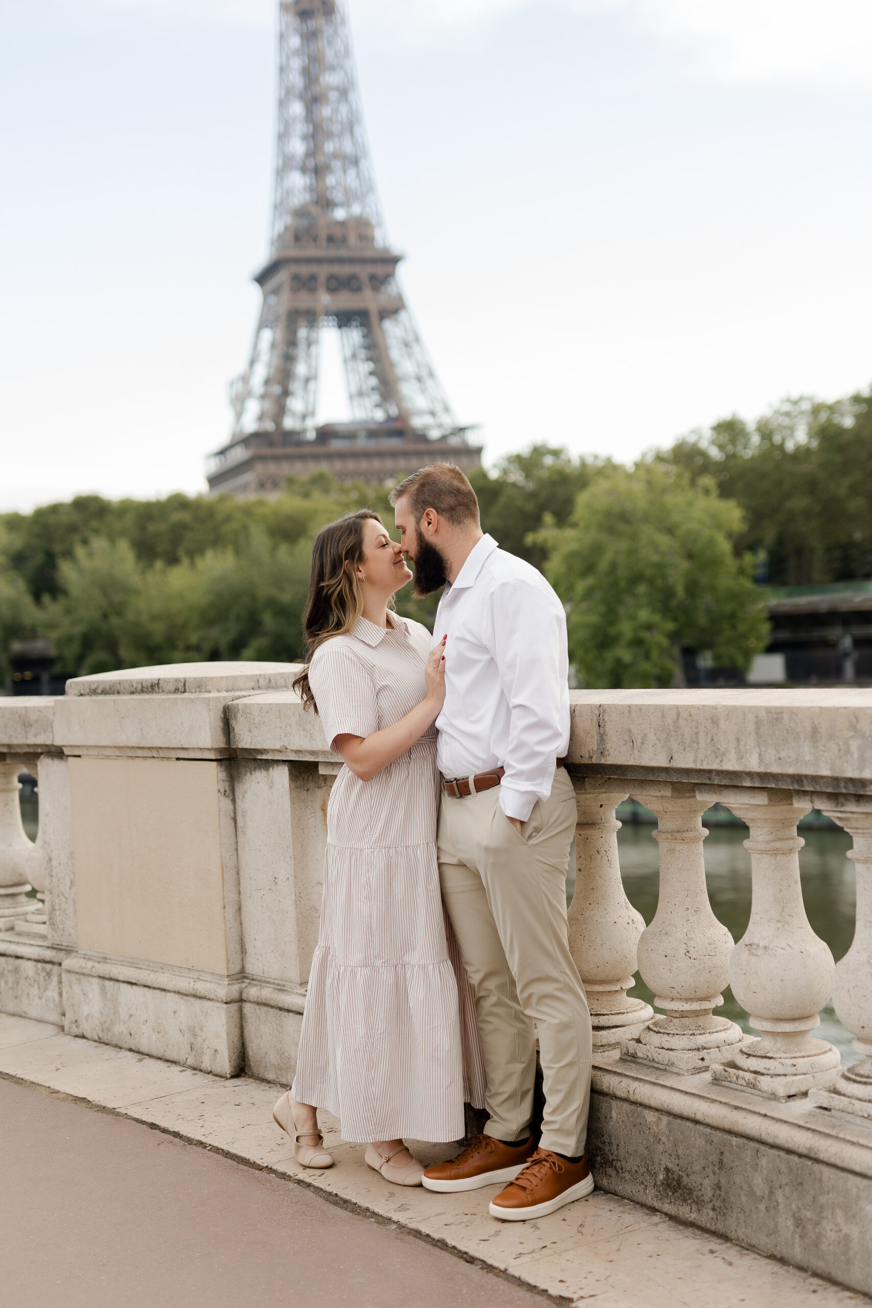 A romantic couple photoshoot on Bir Hakeim Bridge in Paris, captured by Katie Donnelly Photography. The couple is posing under the iconic bridge with the Eiffel Tower in the background.