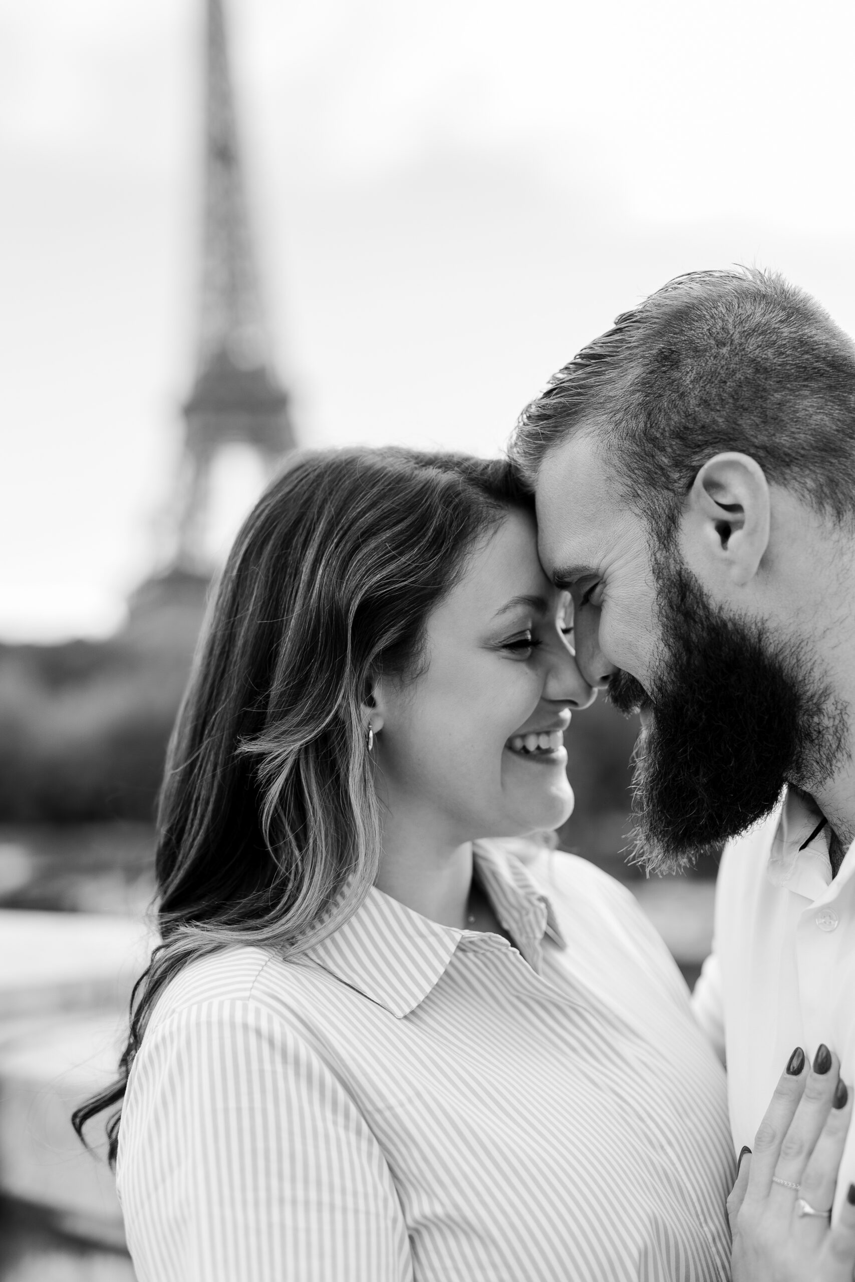 A romantic couple photoshoot on Bir Hakeim Bridge in Paris, captured by Katie Donnelly Photography. The couple is posing under the iconic bridge with the Eiffel Tower in the background.