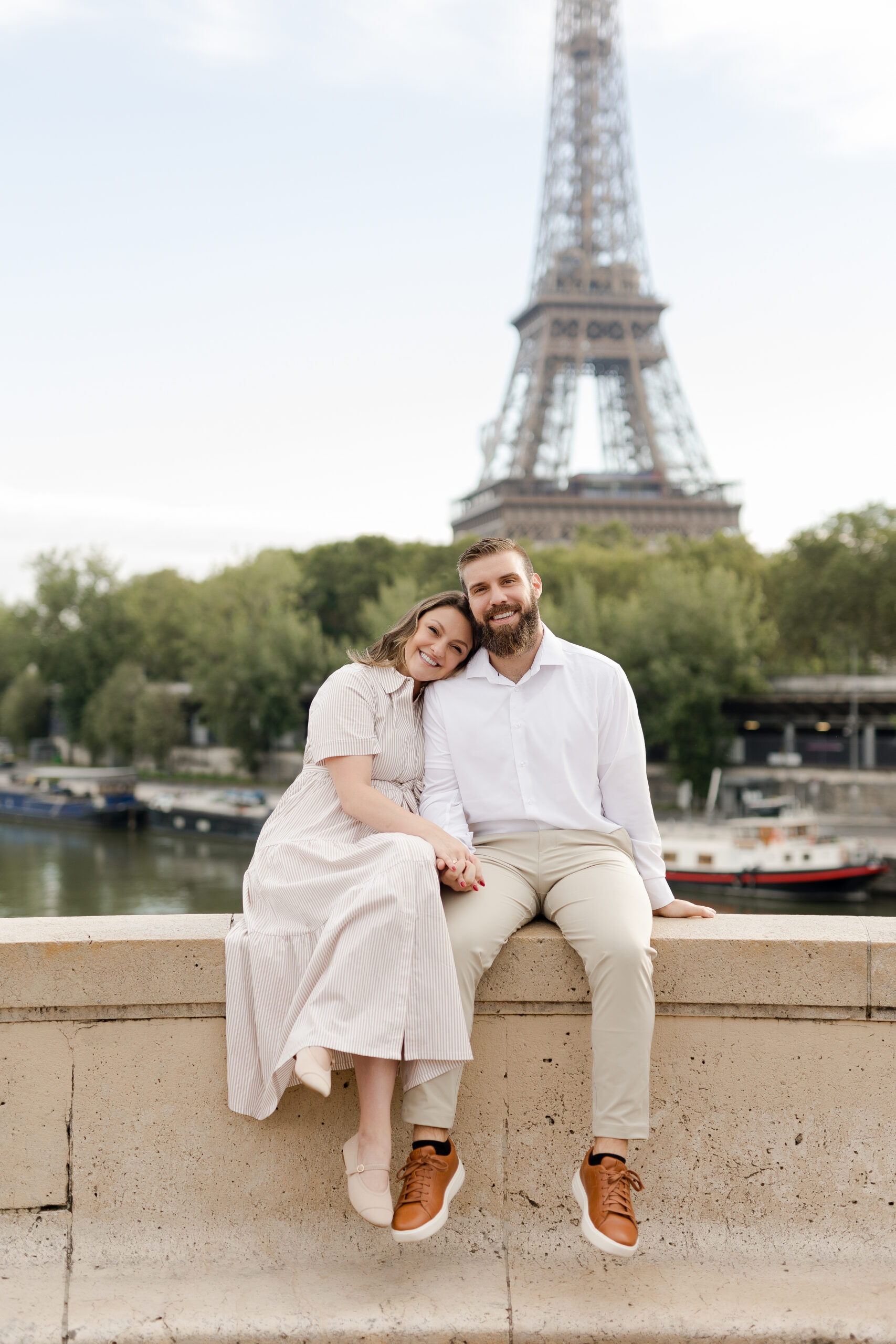 A romantic couple photoshoot on Bir Hakeim Bridge in Paris, captured by Katie Donnelly Photography. The couple is posing under the iconic bridge with the Eiffel Tower in the background.