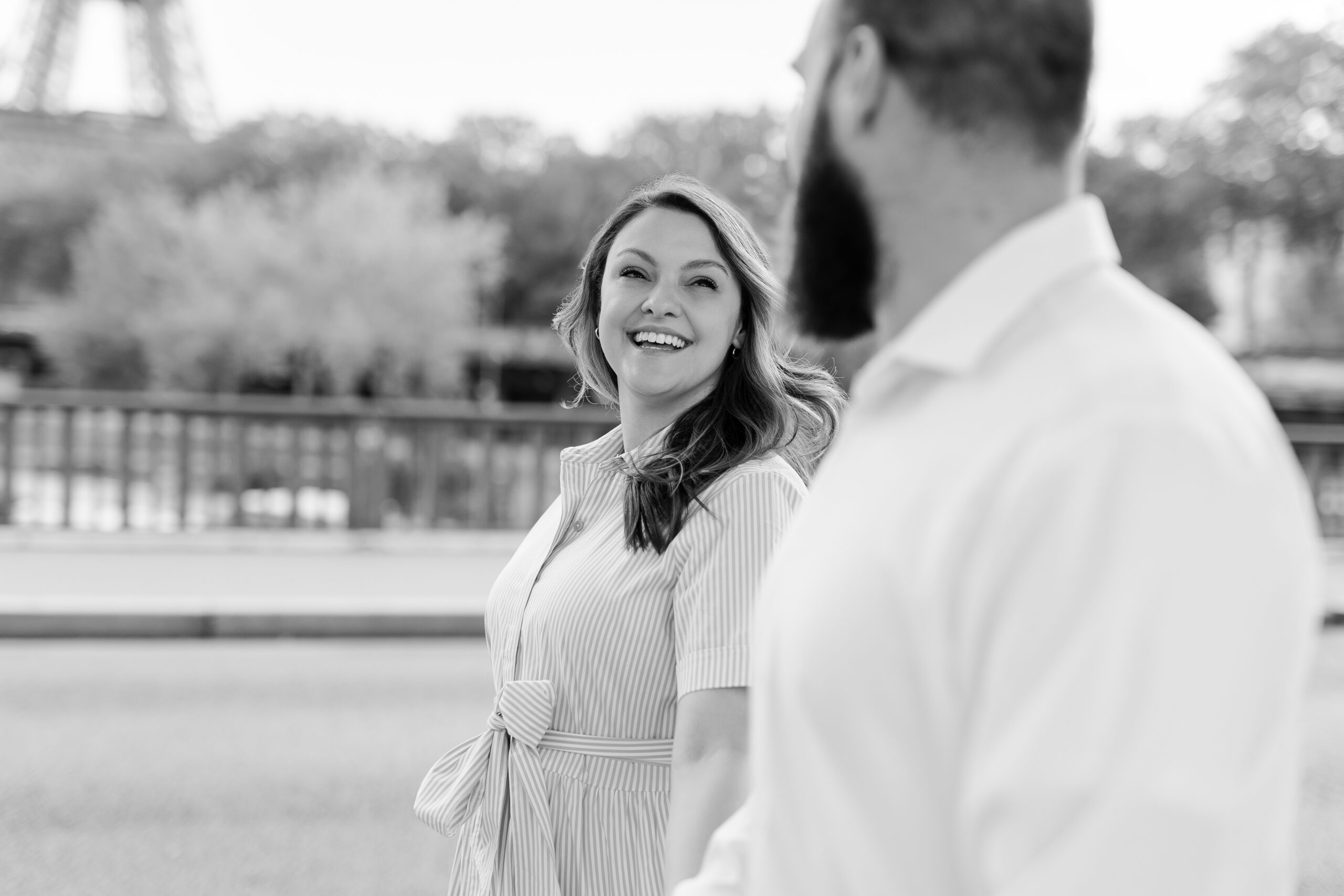 A romantic couple photoshoot on Bir Hakeim Bridge in Paris, captured by Katie Donnelly Photography. The couple is posing under the iconic bridge with the Eiffel Tower in the background.