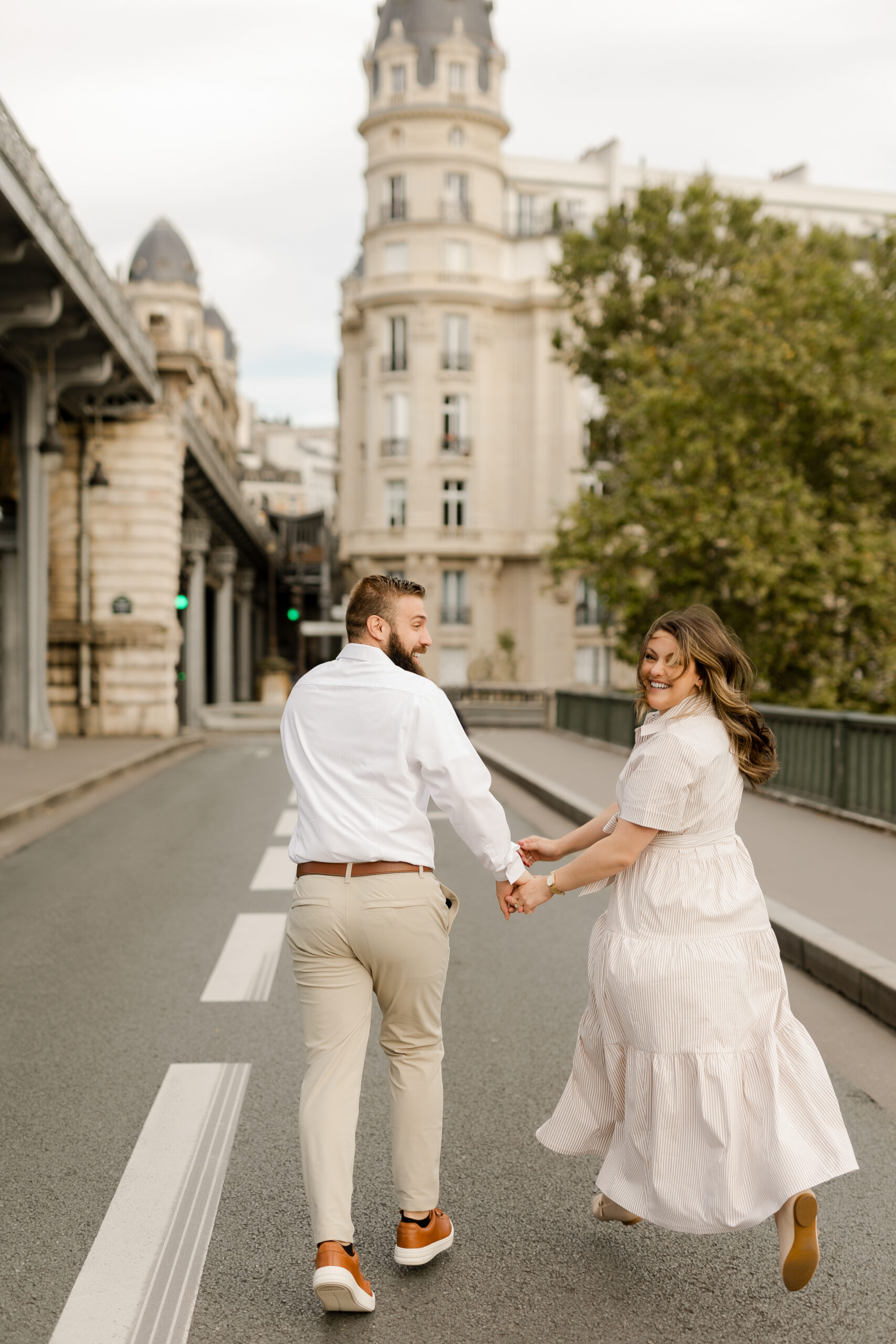 A romantic couple photoshoot on Bir Hakeim Bridge in Paris, captured by Katie Donnelly Photography. The couple is posing under the iconic bridge with the Eiffel Tower in the background.