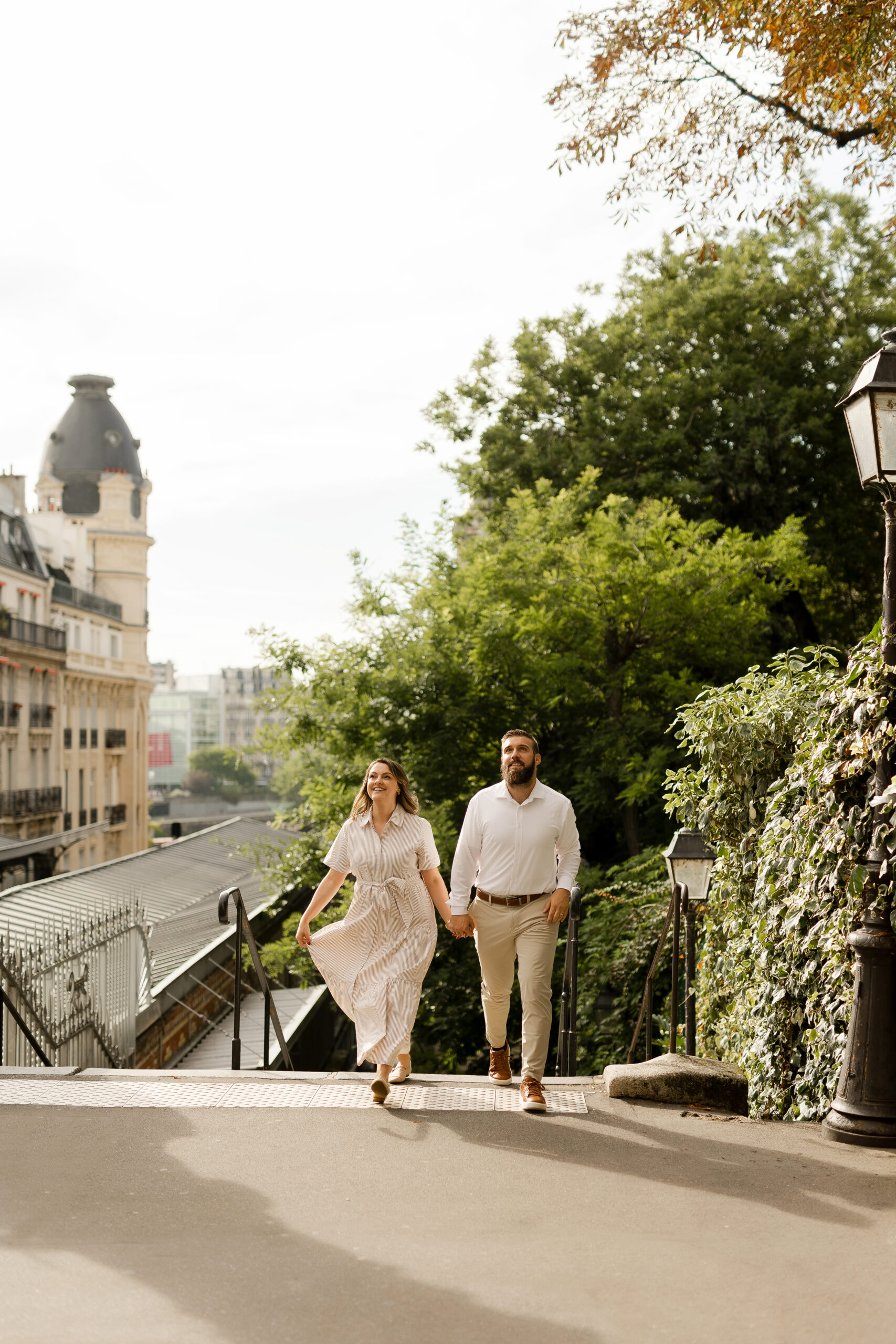 A romantic couple photoshoot on Bir Hakeim Bridge in Paris, captured by Katie Donnelly Photography. The couple is posing under the iconic bridge with the Eiffel Tower in the background.