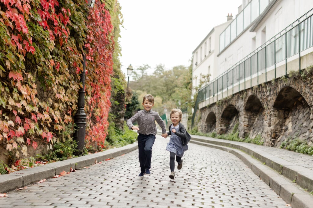 Portrait of two young kids running through streets of Montmartre in September in Paris by Katie Donnelly Photography