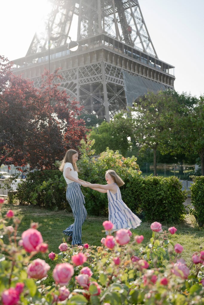 Sisters playing under Eiffel Tower during Spring flower blossoms in Paris by Katie Donnelly Photography