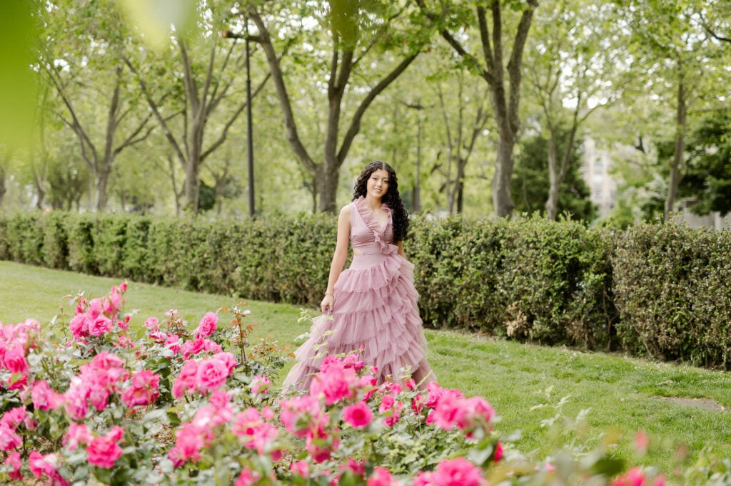 Portrait of young woman in pink dress walking in Paris park near rose bushes during Spring flower blossom season by Katie Donnelly Photography